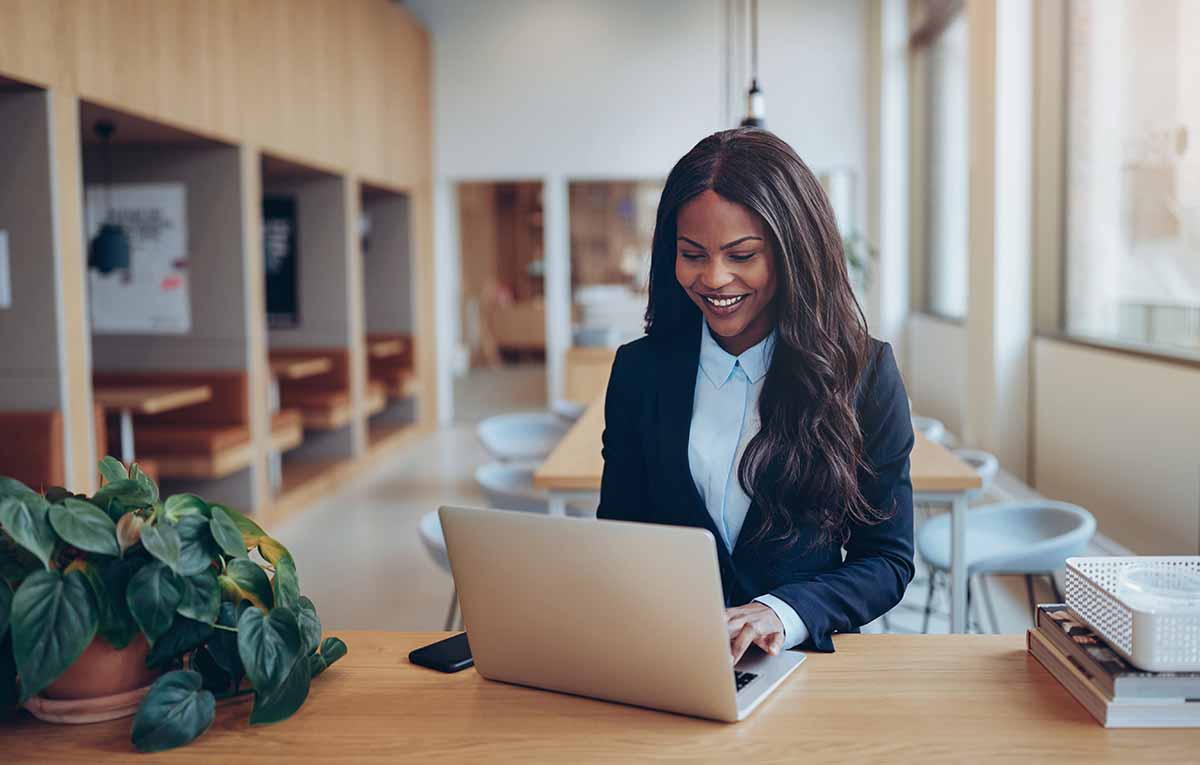 A young African American businesswoman smiling while working on her laptop in an office setting.