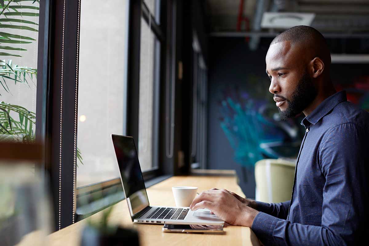 Middle aged African-American sitting by window in a office using a laptop.